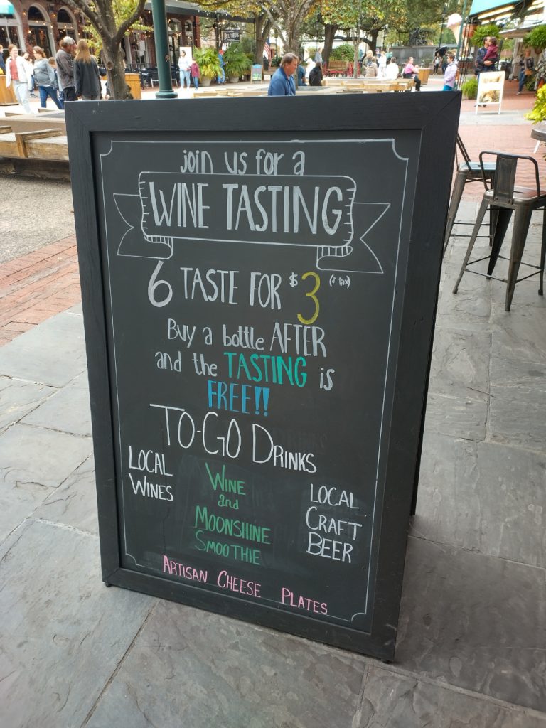 A sidewalk sign advertising a wine tasting in Savannah's City Market area
