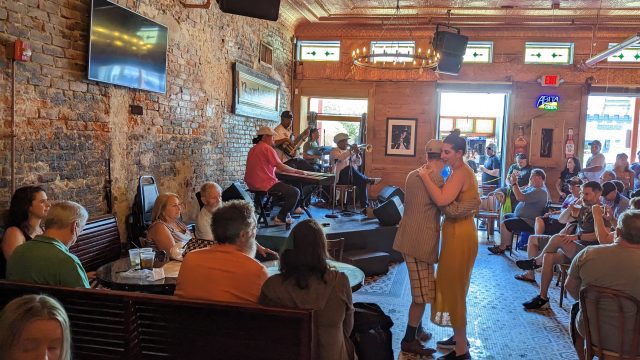 A jazz band performs at a bar while a couple dances.