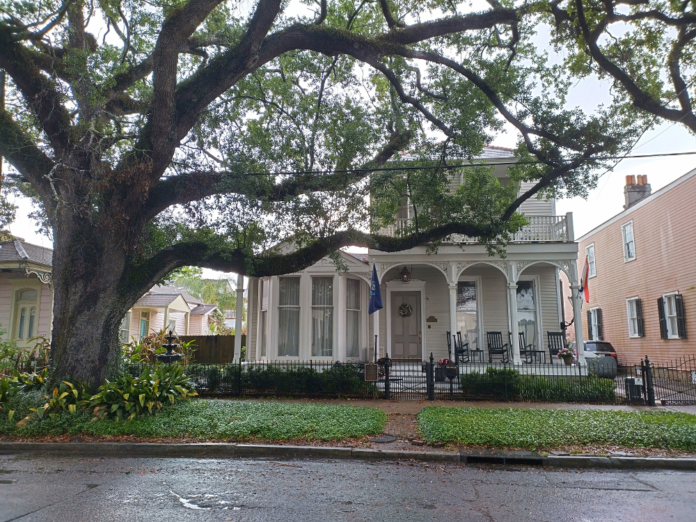 A home with gingerbread columns on the cozy front porch under a large tree.